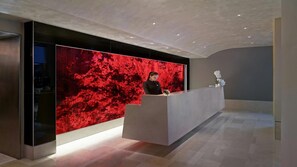 Ein Empfangsbereich im modernen Design mit einer großen, strukturierten roten Wand, einer eleganten Rezeption und einer Vase mit weißen Blumen.