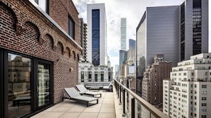 Eine Dachterrasse mit Liegestühlen, ein Backsteinhaus und moderne Wolkenkratzer im Hintergrund.