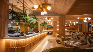 Ein Restaurantinnenraum mit Holzbalkendecke, hängenden Pflanzen und runden Deckenleuchten.