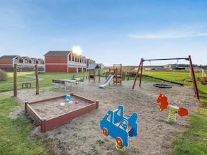 A playground with various play structures, including a swing set and a slide, in a grassy area with a building in the background. - 4 Star Holiday Home in Lokken (Lokken)