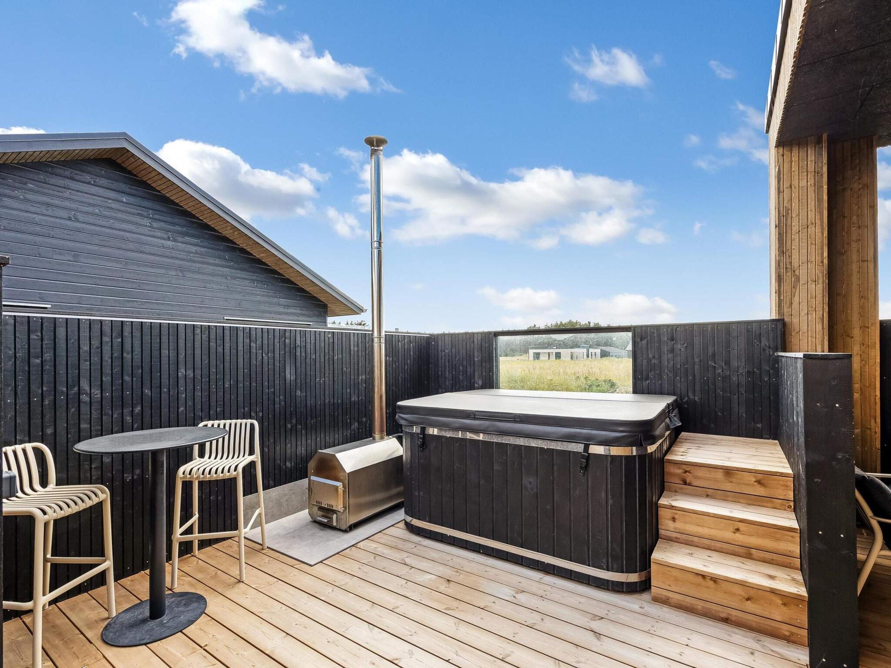 A wooden deck with a hot tub, two chairs, and a table.