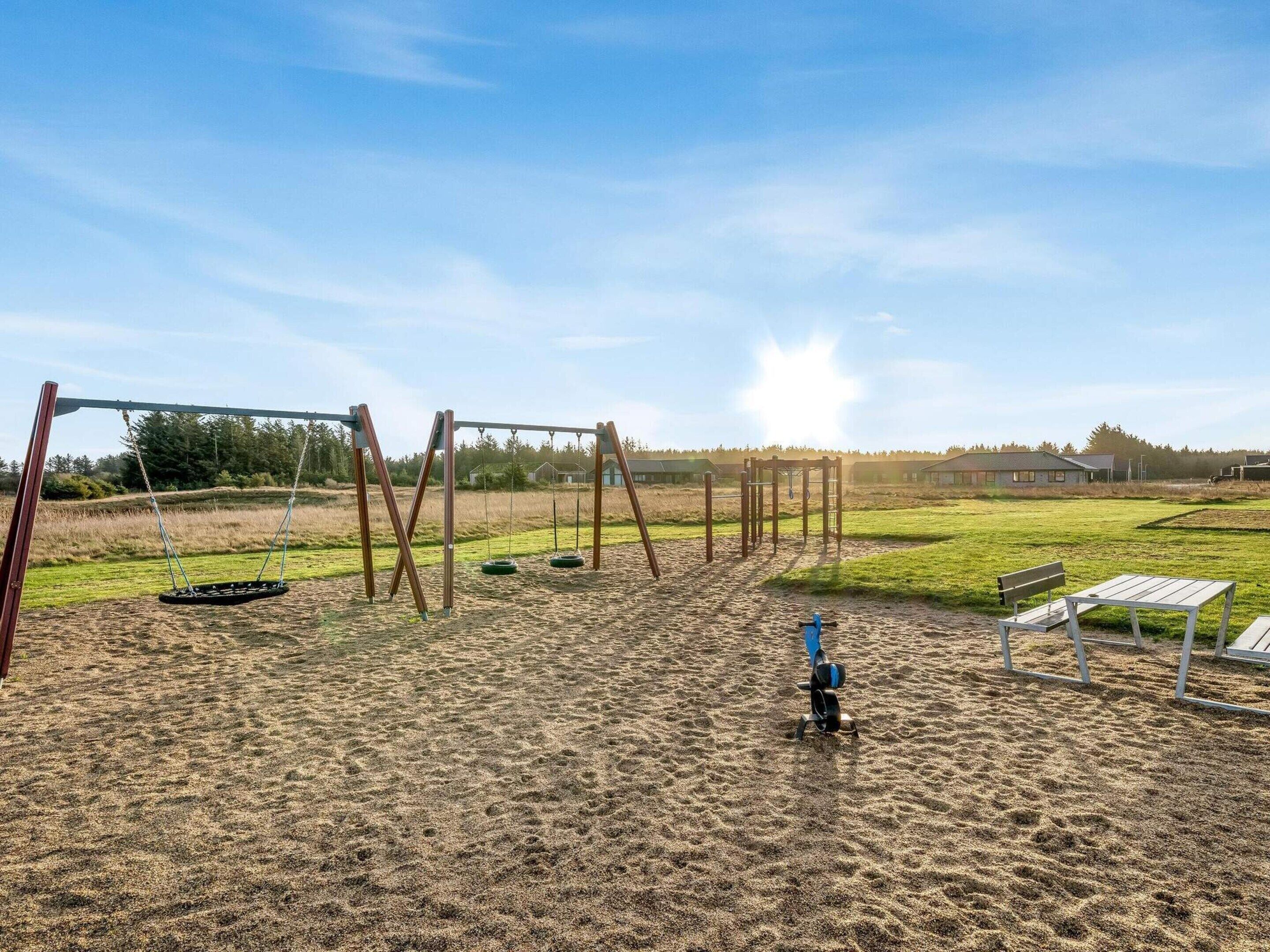 Een speelplaats met schommels en een glijbaan, omgeven door een grasveld en een gebouw op de achtergrond.