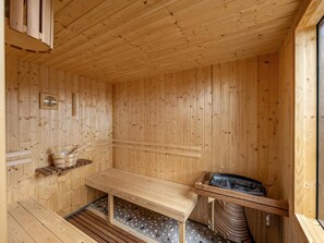 A wooden sauna room with a bench, a heater, and a wooden wall clock. - 4 Star Holiday Home in Lokken (Lokken)