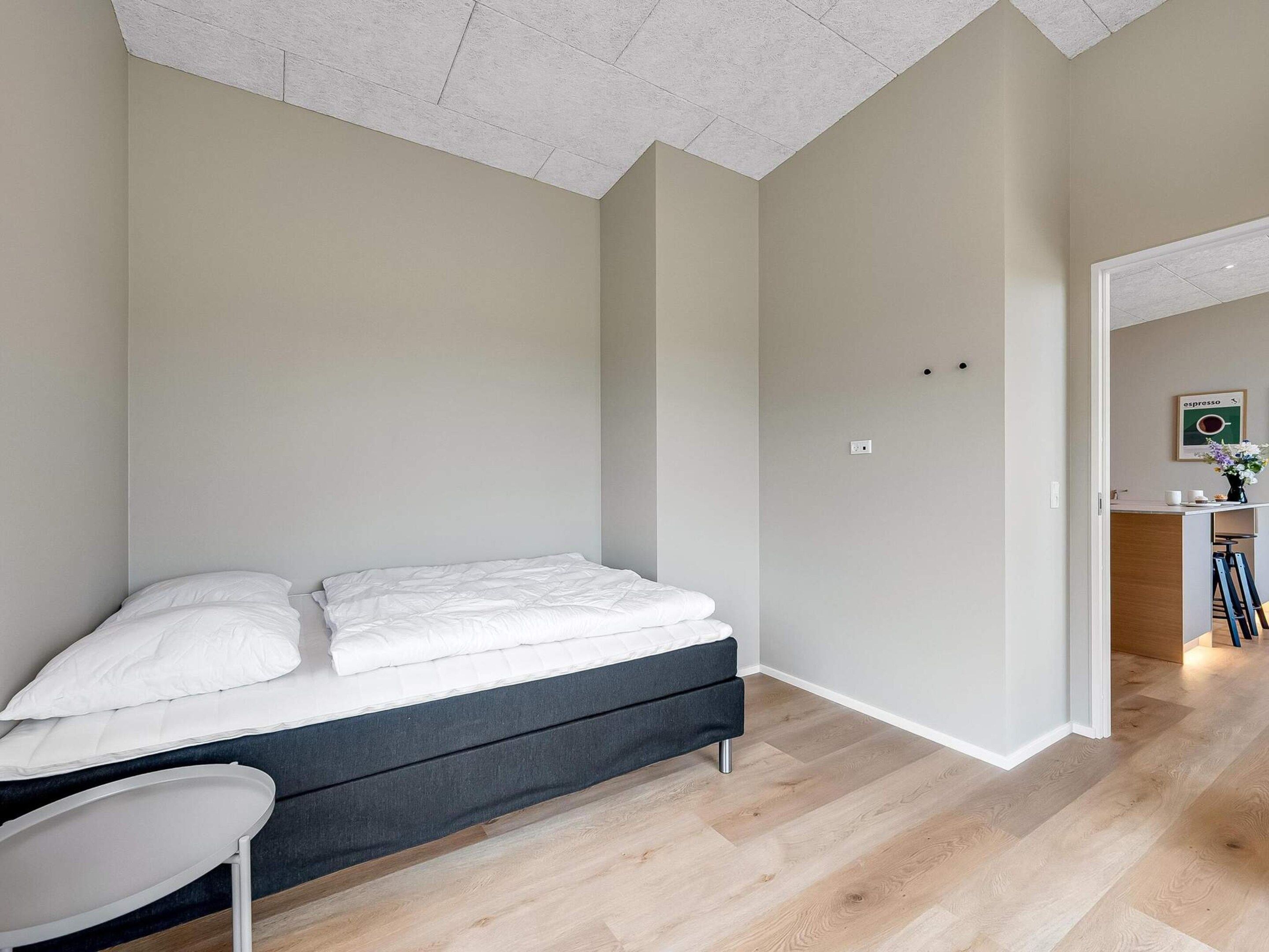 A bedroom with a bed, a chair, and a kitchenette area.