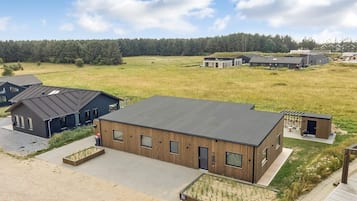 A modern building with a flat roof, surrounded by a grassy field and a forest in the background.