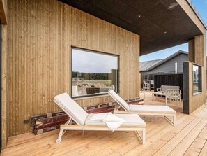 A wooden deck with two lounge chairs, a large window, and a view of a building. - 4 Star Holiday Home in Lokken (Lokken)
