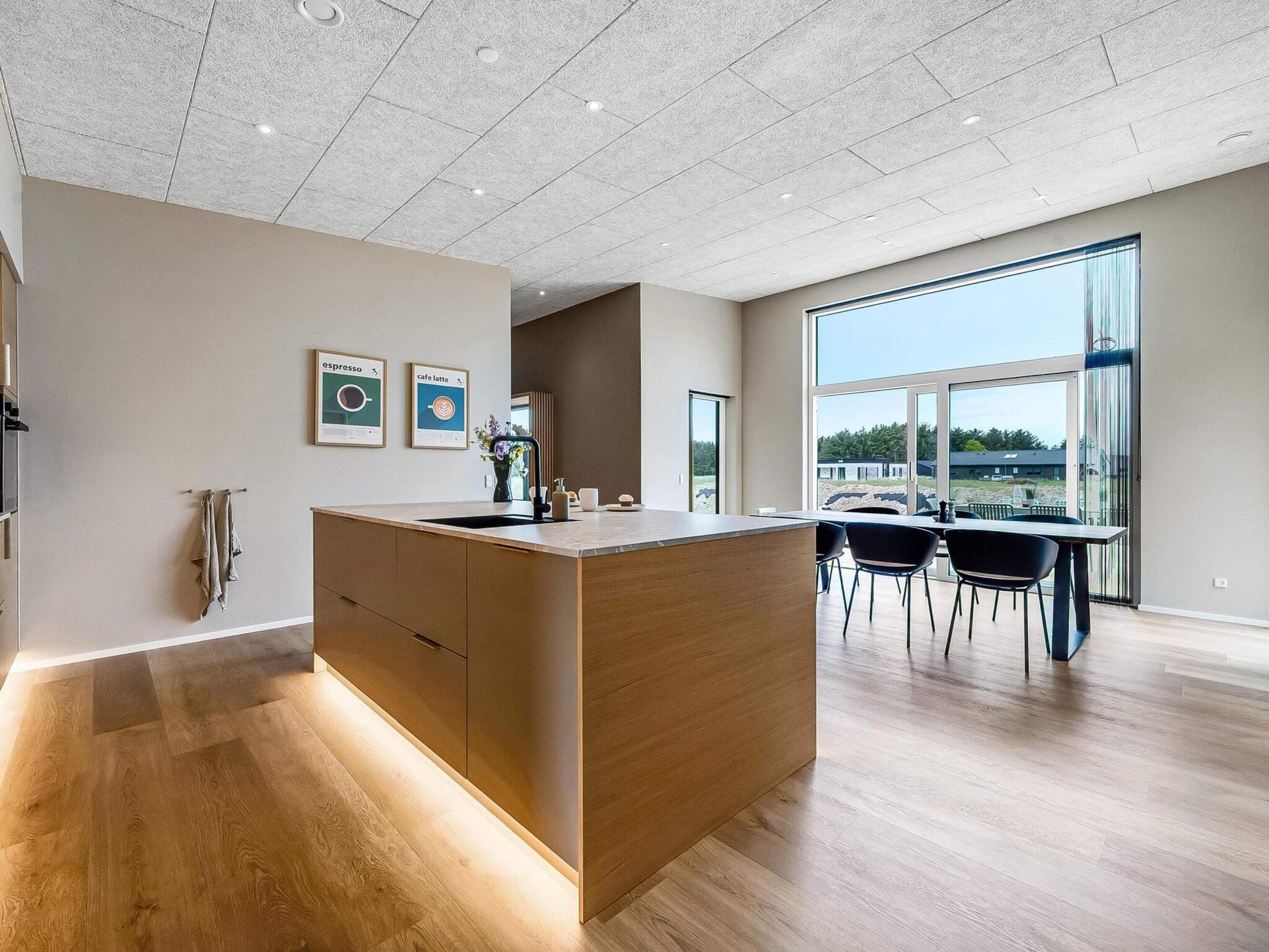 A modern kitchen with a central island, wooden flooring, and a dining area with chairs and a table.