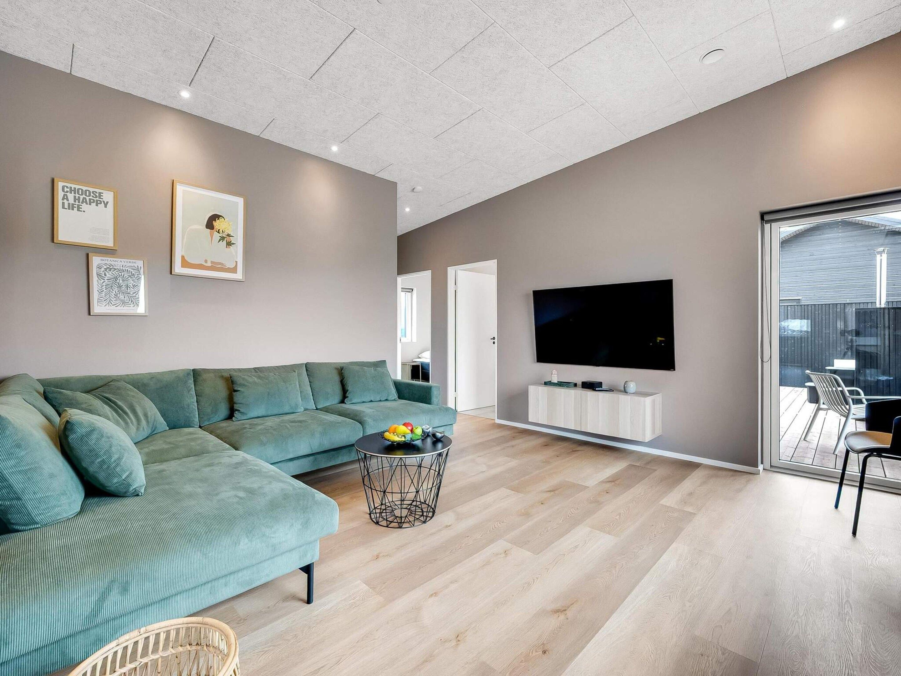 A modern living room with a sectional sofa, a flat-screen TV, and a herringbone-patterned floor.