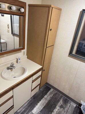 Un baño con un mueble de madera, un lavabo, un espejo y un papel tapiz estampado.