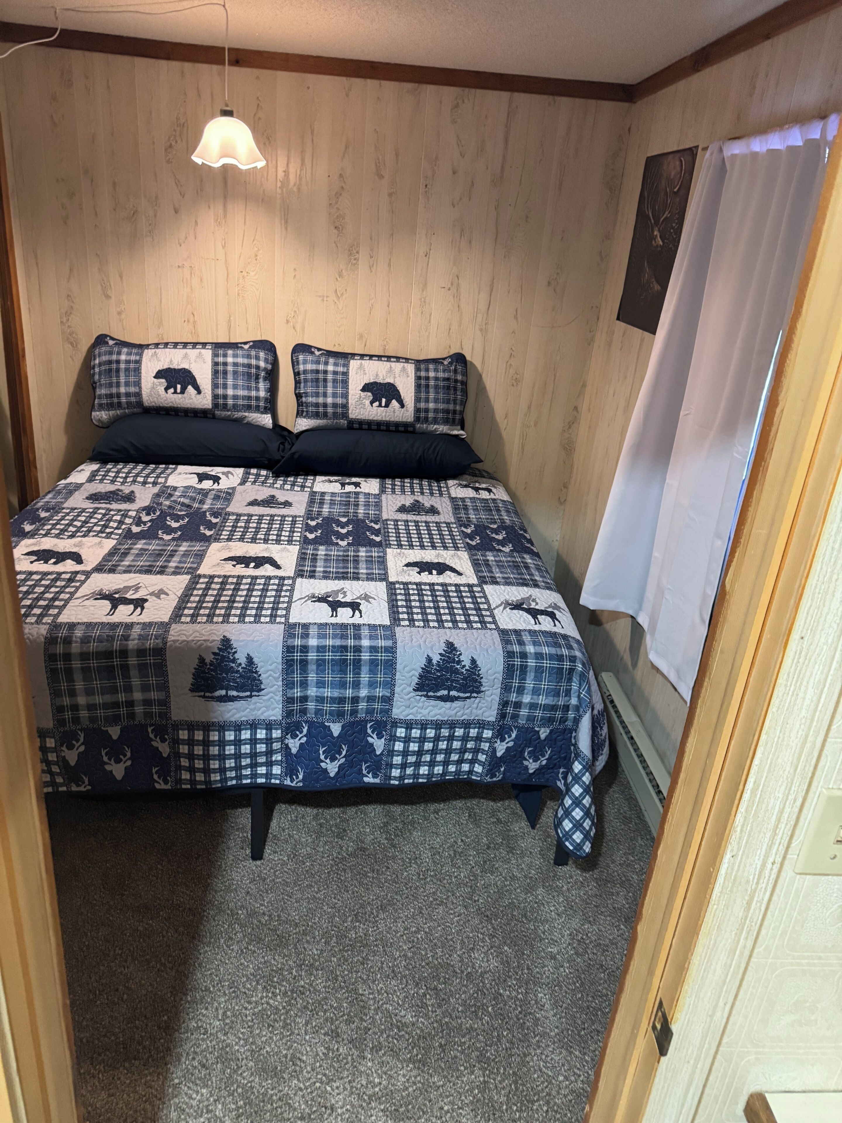 A bedroom with a bed, two pillows, a hanging light, a window with curtains, and a wall with a picture.