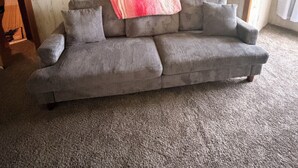 A living room with a gray sofa, a pink blanket, and a mirror reflecting a dining area.