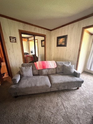 A living room with a gray sofa, a pink blanket, and a mirror reflecting a dining area.