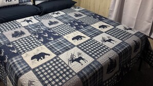 A bedroom with a quilted bedspread featuring animal patterns, a hanging light fixture, and a wall-mounted painting.
