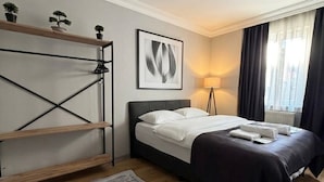 A hotel room with a bed, a standing desk, a floor lamp, and a large window with curtains. - Lotus Suite Otel (Balıkesir)