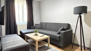 A modern living room with a sofa, ottoman, coffee table, floor lamp, and a ceiling light fixture. - Lotus Suite Otel (Balıkesir)