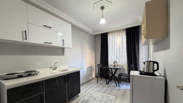 A modern kitchen with a white countertop, black cabinets, a built-in stove, and a refrigerator. - Lotus Suite Otel (Balıkesir)