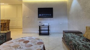 Een moderne woonkamer met een flatscreen-televisie aan de muur, een bank, een salontafel en een eethoek met stoelen.