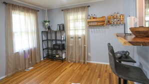 A room with wooden flooring, a black shelving unit with kitchen appliances, a wooden table with a bowl, and a chair. - Wonderful 2-bedroom house in charming Augusta (Augusta)