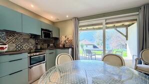 A modern kitchen with a dining area, a microwave, oven, and a view of the outdoors. - Grand T3 en Rez-de-jardin Tresserve (Tresserve)
