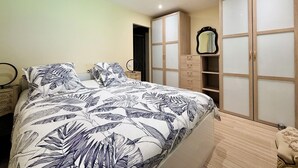 A bedroom with a bed, a nightstand, a mirror, and a wardrobe with sliding doors. - Grand T3 en Rez-de-jardin Tresserve (Tresserve)