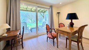 A room with a wooden table, two chairs, a lamp, and a view through a glass door to an outdoor area with chairs and greenery. - Grand T3 en Rez-de-jardin Tresserve (Tresserve)