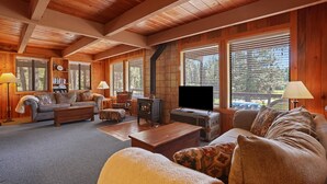 A cozy living room with a fireplace, wooden walls, and large windows. - Rivers Edge, 3 bedroom cabin with River Access (Garden Valley)