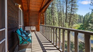A wooden deck with a railing, two chairs, and a bench with cushions. - Rivers Edge, 3 bedroom cabin with River Access (Garden Valley)