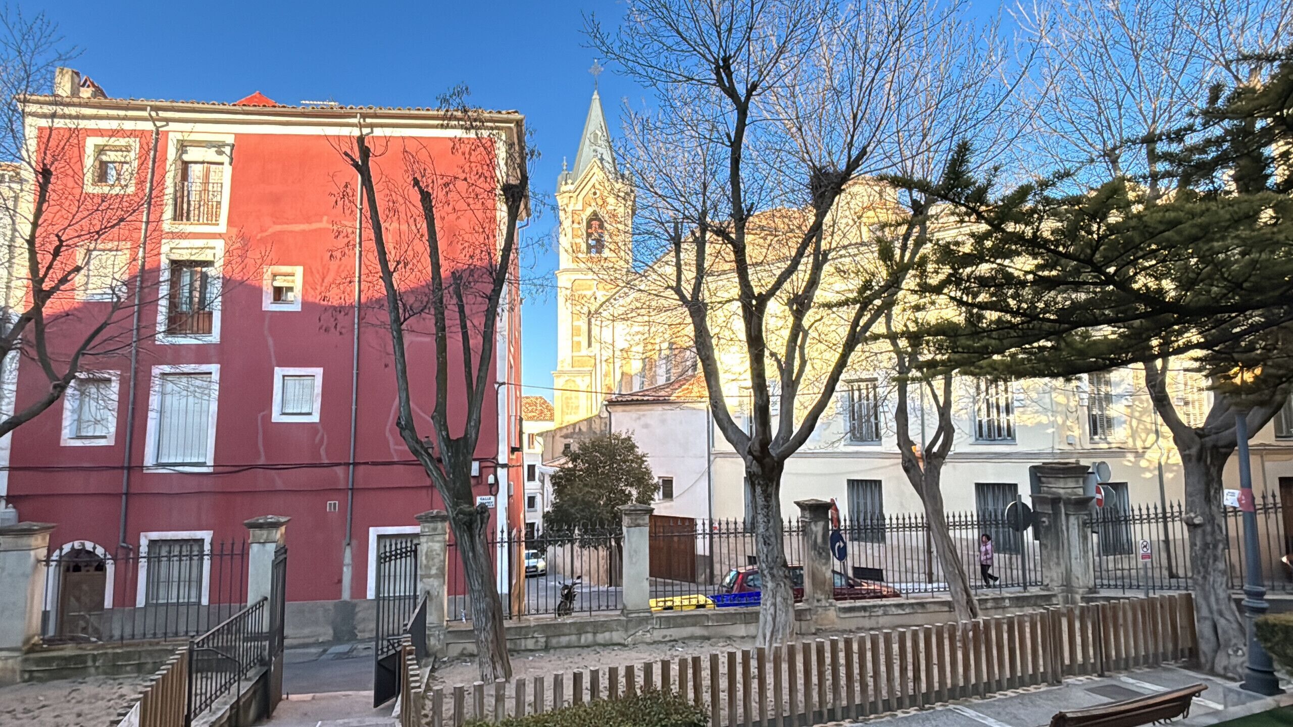 Eine Straße mit Gebäuden, einem Kirchturm und kahl stehenden Bäumen.