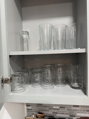 A kitchen cabinet with two shelves containing clear glass jars and cups.