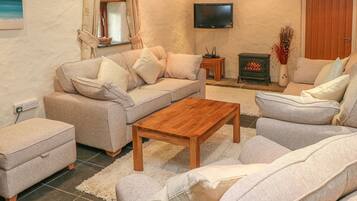 A living room with a sofa, ottoman, coffee table, fireplace, TV, and a window with curtains.