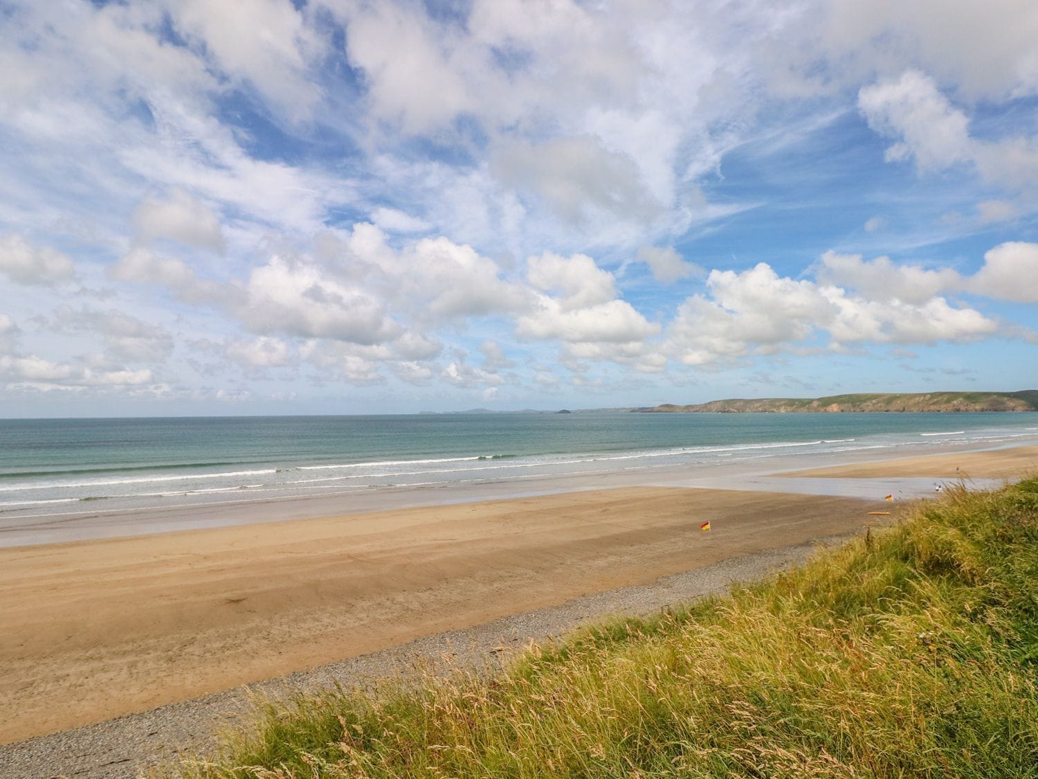 A beach with a gravel path, grassy area, and a flag.