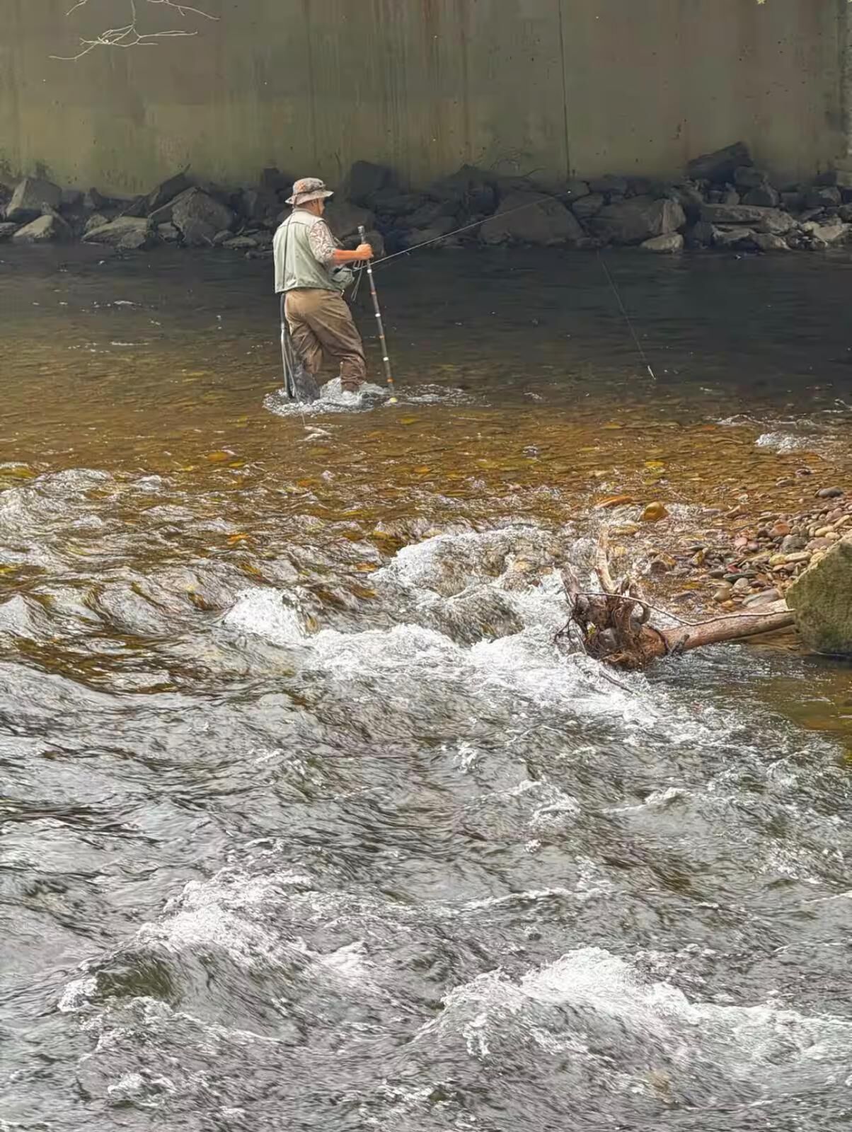 A person standing in a river with a fishing rod.