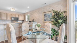 A modern kitchen with wooden cabinets, a microwave, and a dining area with a glass table and chairs. - By The Lake Resort Access (Lake Ozark)