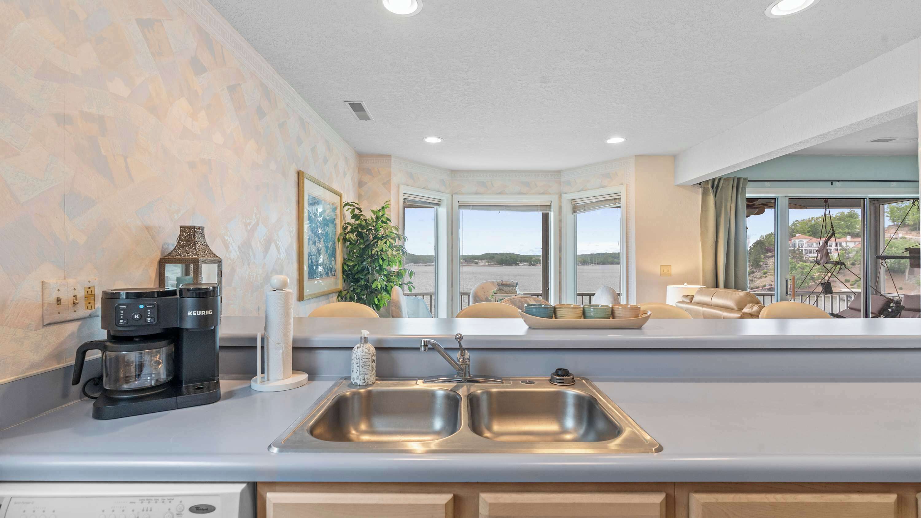 A kitchen with a double sink, a coffee maker, and a view of the outdoors.