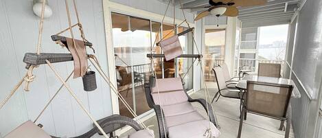 A balcony with wicker chairs and a swing, a ceiling fan, and a view of the city.