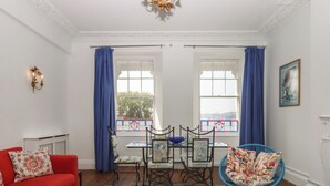 Ein Zimmer mit einem roten Sofa, einem blauen Sessel, einem Tisch mit einer blauen Schüssel und einem Fenster mit blauen Vorhängen.