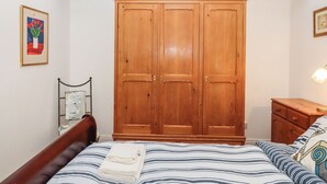 Ein Schlafzimmer mit einem Bett, einem Holzschrank, einem Nachttisch und einem gerahmten Bild an der Wand.