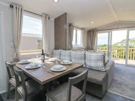 Un comedor con una mesa de madera preparada para cuatro personas, asientos acolchados y ventanas amplias con vistas al paisaje.