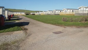 Un parque para caravanas con un camino de grava que lleva a varias caravanas, un área verde y un cielo despejado.