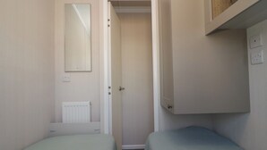 Una habitación pequeña con dos camas individuales, una puerta que da a otra habitación, un radiador y un espejo en la pared.