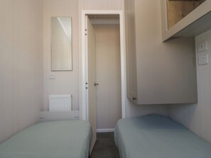 A small room with two single beds, a door leading to another room, a radiator, and a mirror on the wall.