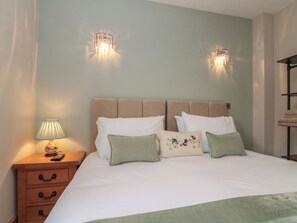Un lit bien fait, avec du linge de lit blanc et plusieurs oreillers, une table de chevet avec une lampe, et deux appliques murales.