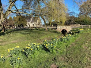 A historic building with stone architecture, a grassy area with daffodils, and a stone bridge. - Bumble Bee Lodge (Filey)