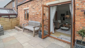 A brick house with a patio, a wooden bench, and a sliding glass door leading to a living area. - Bumble Bee Lodge (Filey)