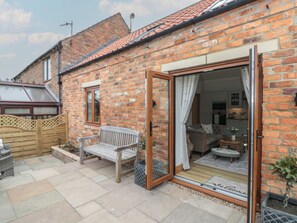 A brick house with a patio, a wooden bench, and a sliding glass door leading to a living area. - Bumble Bee Lodge (Filey)