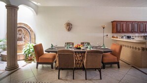 Zona pranzo con tavolo rotondo, quattro sedie, un elemento decorativo a parete e angolo cottura con pensili in legno.