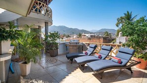 Una terrazza sul tetto con poltrone relax, un barbecue, piante in vaso e vista sulle montagne.