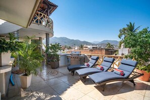 A rooftop terrace with lounge chairs, a grill, potted plants, and a view of mountains. - 7 Private King Suites-Rooftop Oasis -Walk to Beach (Puerto Vallarta)