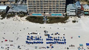 A beach resort with multiple swimming pools, a large hotel building, and numerous beach umbrellas and lounge chairs.