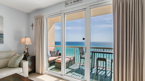 A room with a view of the ocean, a sofa, a lamp, and a sign reading 'Gulf of America.'